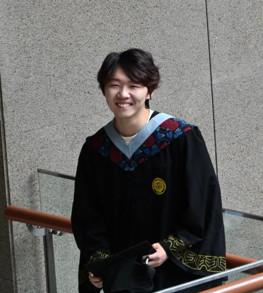 Student wearing their graduation gown and posing for a picture. 